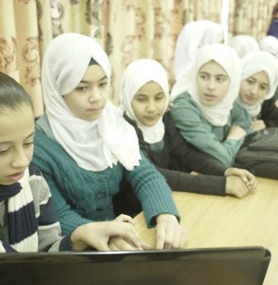 Students at a Jordan high school gather around a laptop to interact with students in Kentucky.