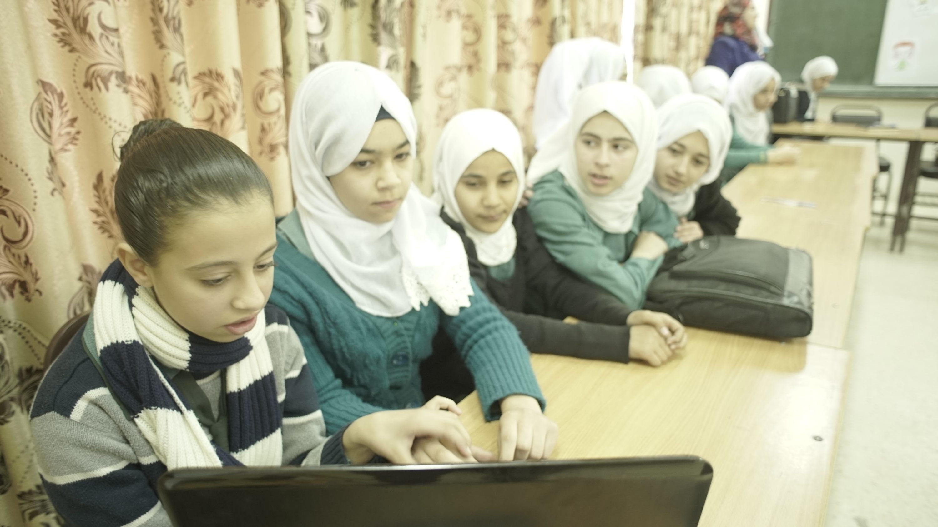 Students at a Jordan high school gather around a laptop to interact with students in Kentucky.