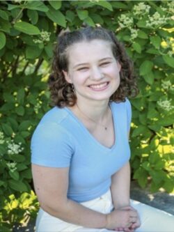 Young woman sitting down in front of a large bush