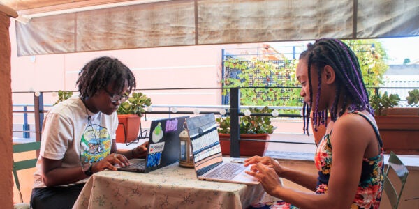 Two young people sitting across from each other at a table working on laptops.