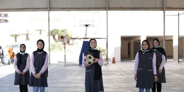A group of young women standing together for a photo. One woman in the center is holding a soccer ball.
