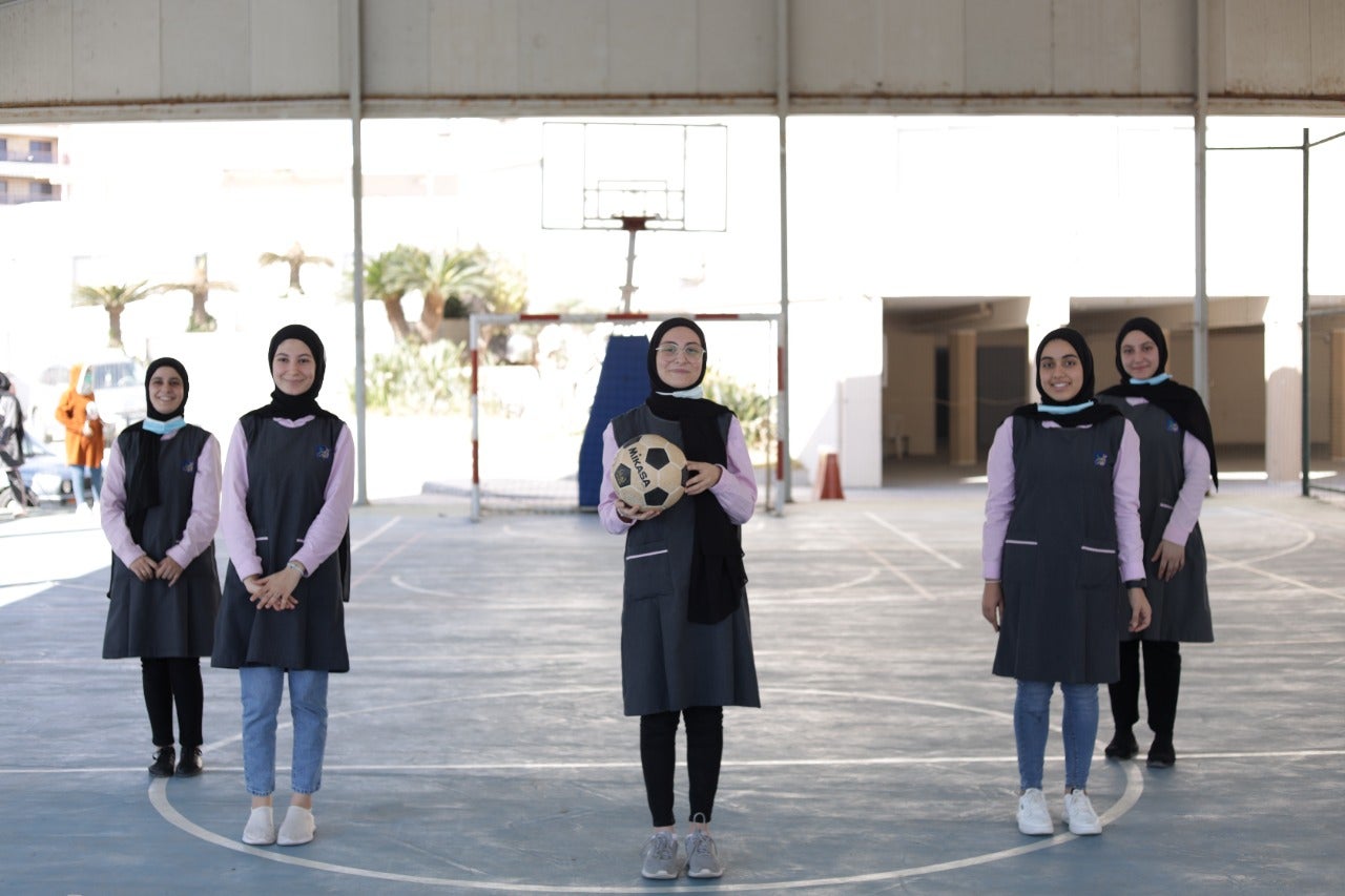 A group of young women standing together for a photo. One woman in the center is holding a soccer ball.